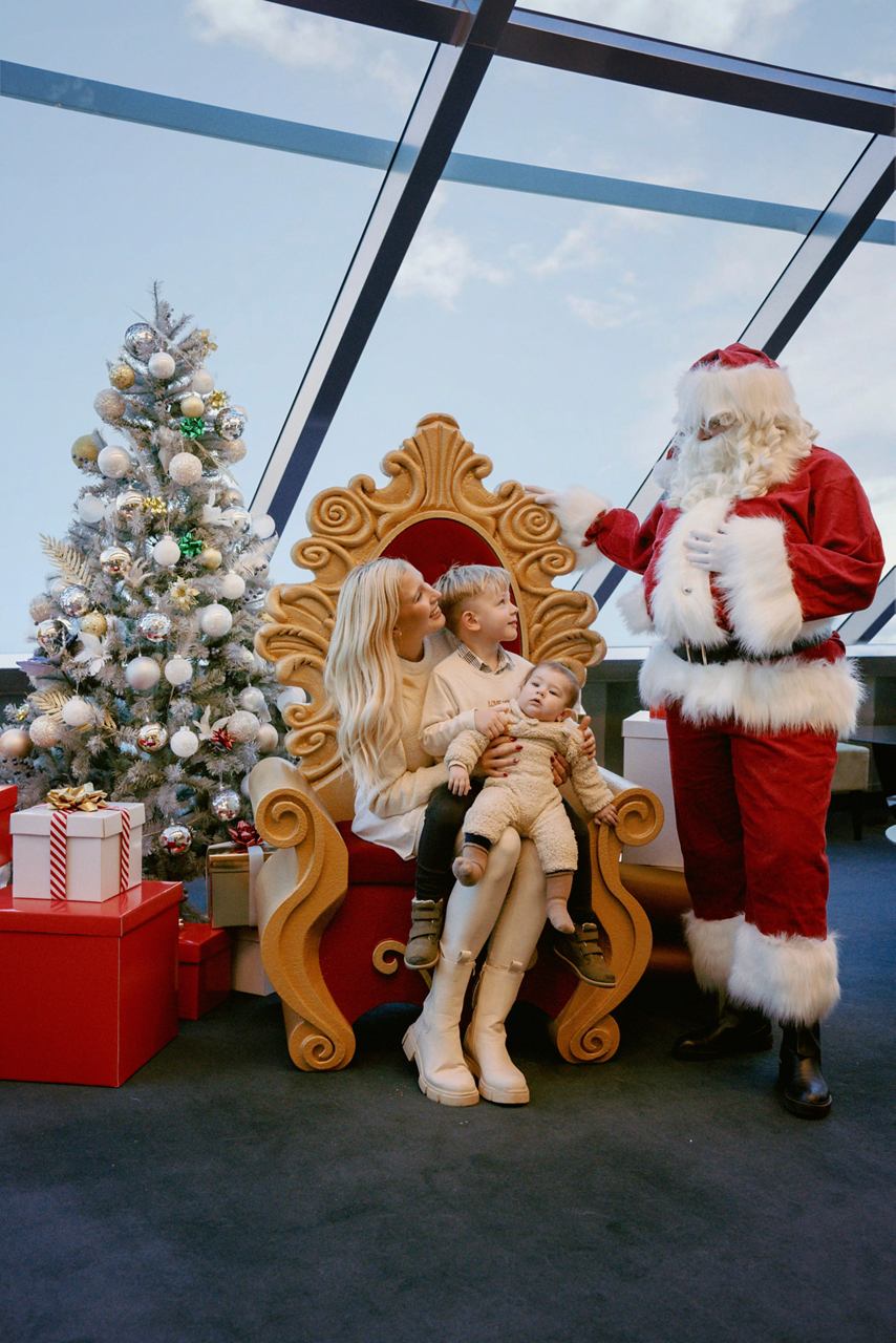 Eine Familie genießt einen festlichen Moment mit dem Weihnachtsmann neben einem geschmückten Weihnachtsbaum und Geschenken an Bord von MSC Virtuosa | MSC Cruises
