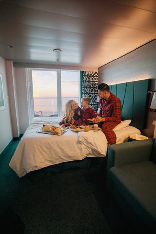 Una familia disfrutando de un desayuno navideño en su cabina, con vista al amanecer sobre el mar desde el balcón | MSC Cruceros