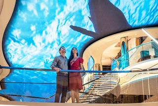 Una pareja disfruta de la vibrante atmósfera del paseo interior bajo la pantalla LED del MSC World Europa | MSC Cruceros