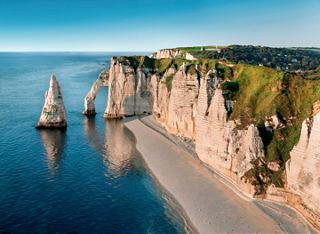 Une vue à couper le souffle des falaises d'Etretat le long de la côte au crépuscule, avec des eaux calmes en dessous | MSC Cruises