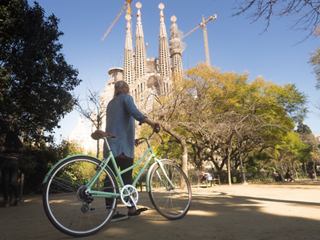 Eine Frau genießt eine Radtour in der Nähe der Sagrada Familia in Barcelona, umgeben von Bäumen und strahlend blauem Himmel | MSC Cruises