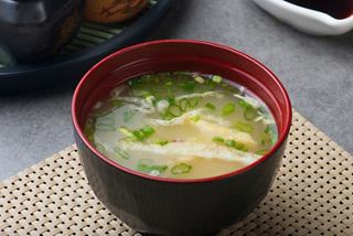 A bowl of miso soup garnished with green onions, served in a traditional red dish | MSC Cruises