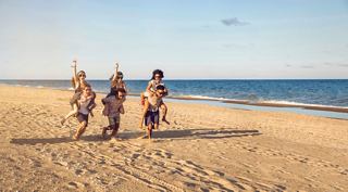 Eine Gruppe von Freunden läuft fröhlich entlang eines Sandstrandes am Meer und schafft gemeinsam unvergessliche Momente | MSC Cruises