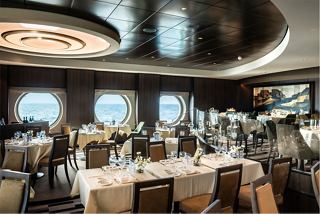 A spacious restaurant on MSC Euribia featuring elegant tables and chairs with porthole views of the sea | MSC Cruises