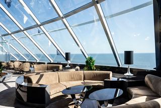 A modern lounge area with large glass walls offering stunning sea views and comfortable seating for relaxation | MSC Cruises