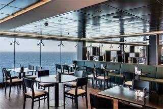 A modern restaurant interior with tables and chairs, featuring a glass wall that offers a view of the sea | MSC Cruises