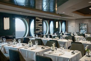 A beautifully arranged restaurant setting with elegant tables and chairs, featuring portholes overlooking the sea | MSC Cruises