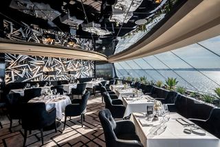 An elegant dining area in the MSC Yacht Club, featuring tables and chairs with panoramic sea views | MSC Cruises