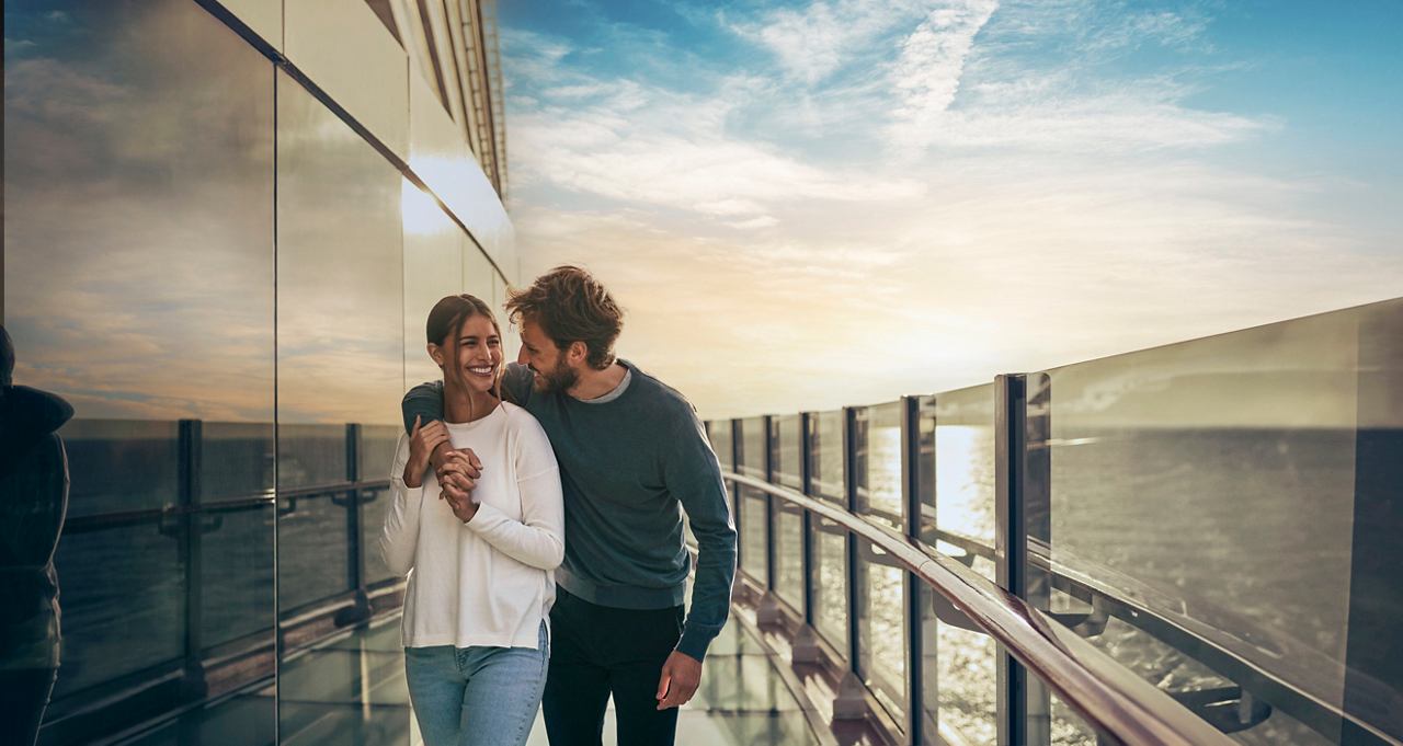 Ein Paar genießt eine warme Umarmung auf der Infinity Bridge der MSC Seashore mit Blick auf das Meer bei Sonnenuntergang | MSC Cruises