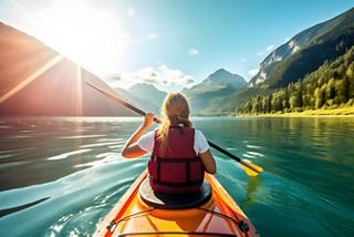 Woman paddling a kayak on a serene lake surrounded by mountains and sunlight | MSC Cruises