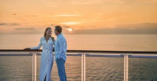 A couple enjoys a romantic moment together by the balustrade with the sea and sunset in the background | MSC Cruises
