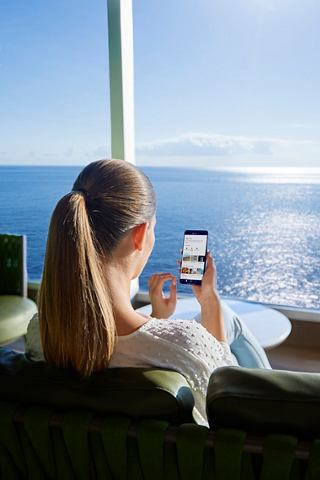 A woman enjoys a serene view of the sea while using her smartphone on board MSC Seashore | MSC Cruises