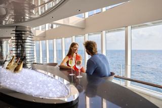 A couple enjoys champagne and conversation while overlooking the sea through a glass wall | MSC Cruises