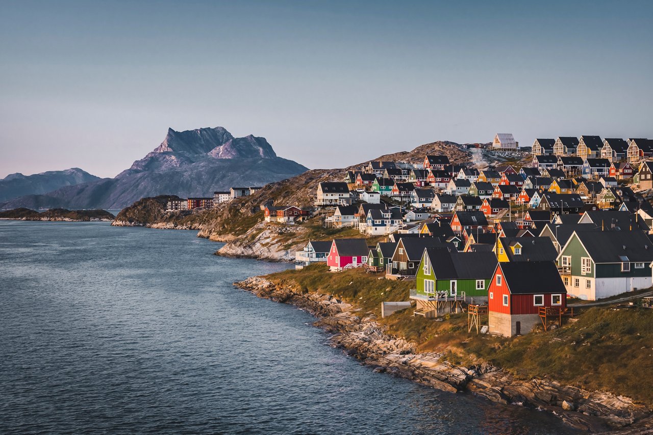A serene coastal view of Nuuk in Greenland, showcasing colourful houses against a majestic mountain backdrop | MSC Cruises
