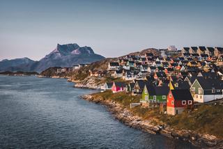 A serene coastal view of Nuuk in Greenland, showcasing colourful houses against a majestic mountain backdrop | MSC Cruises