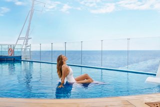 A woman relaxes by the infinity pool with a stunning sea and sky backdrop | MSC Cruises