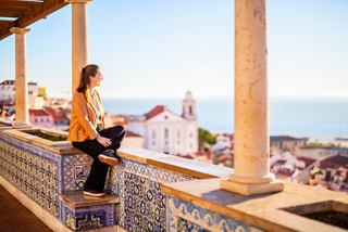 A woman enjoys a panoramic view of the sea and architecture while sitting on a balcony in Funchal, Portugal | MSC Cruises