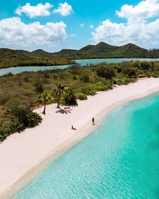 Luftaufnahme eines Paares, das an einem ruhigen Strand mit türkisfarbenem Meer und üppigem Grün in Antigua spaziert | MSC Cruises