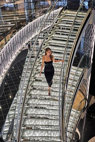 A woman in a stylish dress gracefully walks down the stairs, enjoying life aboard MSC Seashore | MSC Cruises