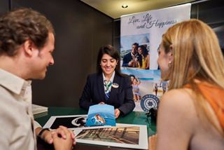 A couple engages with a friendly staff member at a service desk on board MSC Seashore | MSC Cruises