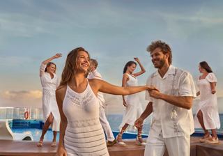 A couple dances joyfully at a vibrant White Party by the infinity pool, surrounded by friends enjoying the entertainment | MSC Cruises