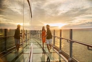 Ein Paar geht fröhlich über die Unendliche Brücke während eines wunderschönen Sonnenaufgangs auf See | MSC Cruises