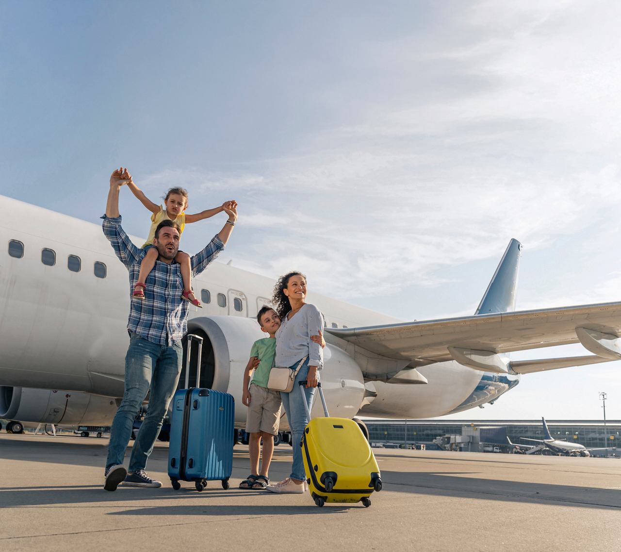 Eine glückliche Familie bereitet sich am Flughafen auf ihre Reise vor, lächelnd mit Gepäck neben einem Flugzeug | MSC Cruises