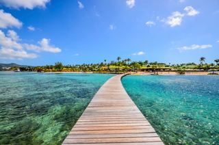 Ein Holzsteg führt zu klaren türkisfarbenen Gewässern und einem sonnigen Strand in Sainte-Anne, Martinique | MSC Cruises