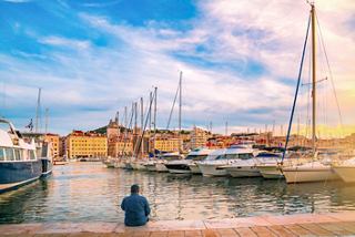 A serene view of a marina in Marseille with colourful buildings and a man sitting peacefully by the water | MSC Cruises