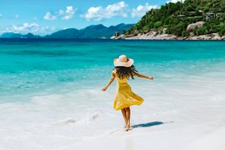 Eine Frau in einem gelben Kleid läuft fröhlich an einem unberührten Strand mit türkisfarbenem Wasser und blauem Himmel entlang | MSC Cruises