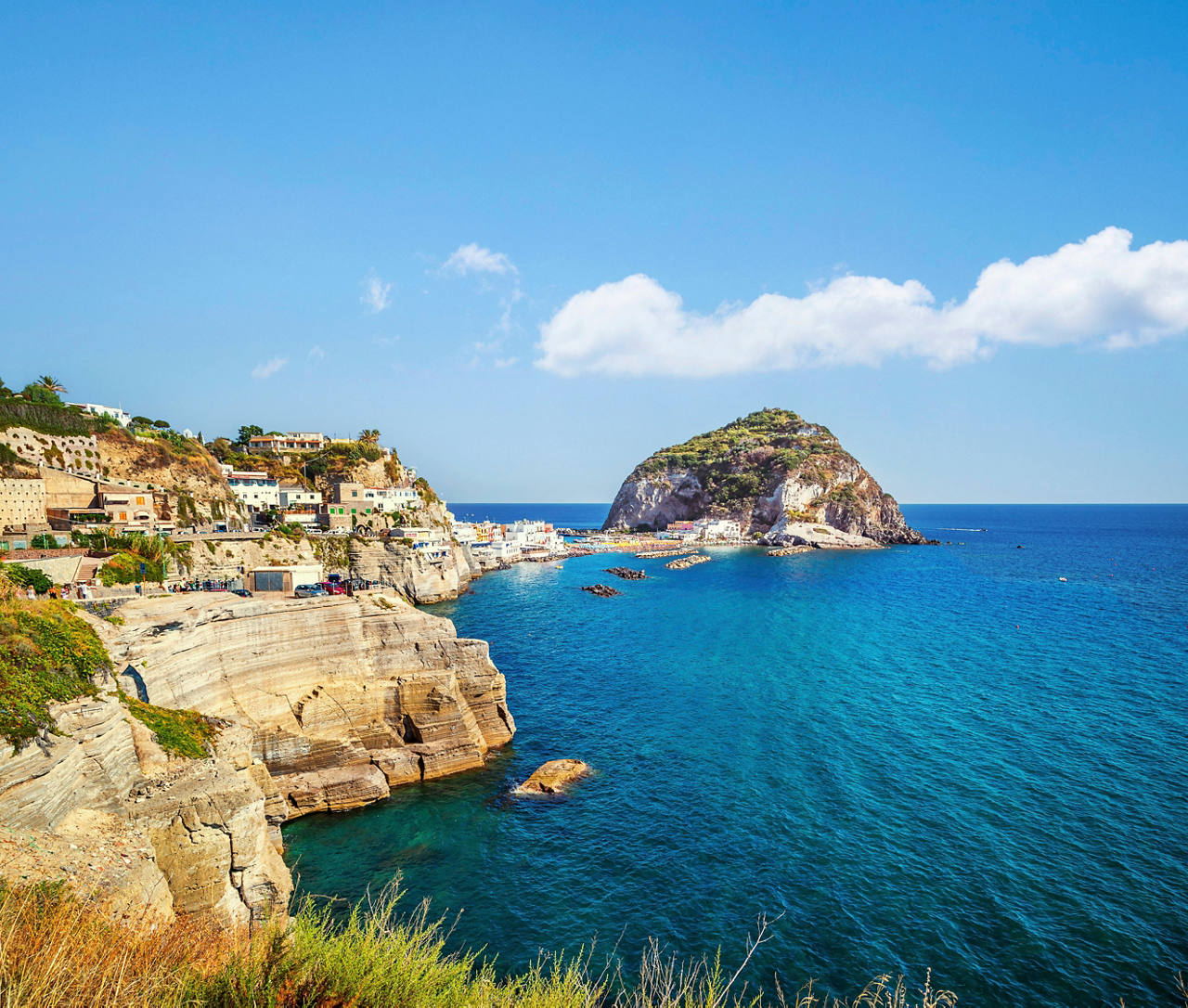 A stunning view of the coastline of Ischia, featuring cliffs, houses, and the vibrant sea under a clear sky | MSC Cruises