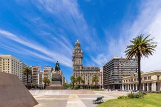 The vibrant Plaza Independencia in Montevideo features Salvo Palace against a bright sky and palm trees | MSC Cruises