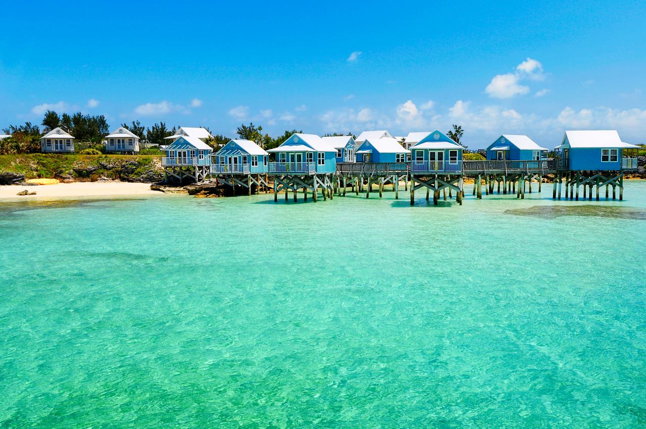 A serene view of a turquoise sea with a sandy beach and lush vegetation under a clear blue sky in Bermuda | MSC Cruises