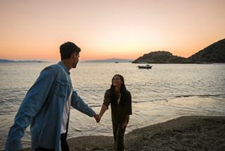 Ein Paar läuft freudig Hand in Hand am Strand bei Sonnenuntergang, mit dem Meer und Hügeln im Hintergrund | MSC Cruises