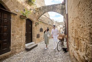 Una pareja pasea por un encantador callejón en Rodas, Grecia, rodeada de arquitectura histórica y paisajes vibrantes | MSC Cruceros