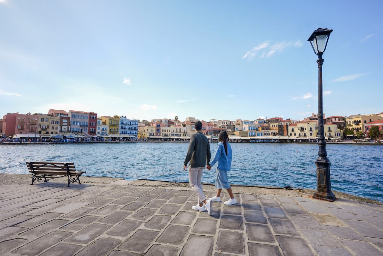 Una pareja disfruta de un momento sereno junto al agua en Chania, Grecia, rodeados de coloridos edificios y mar tranquilo | MSC Cruises