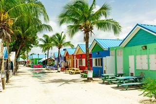A scenic view of colourful beach houses lined along a sandy path, surrounded by palm trees in Barbados | MSC Cruises