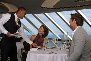 Ein Kellner bedient ein Paar an einem Tisch im MSC Yacht Club Restaurant, umgeben von atemberaubendem Meerblick | MSC Cruises