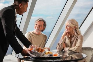 Un mayordomo sirve el desayuno a una pareja mayor que disfruta de su tiempo en el MSC Yacht Club con una vista impresionante | MSC Cruceros