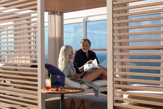 A couple relaxes in a stylish cabana on the MSC Yacht Club Sundeck, enjoying cocktails and the sea view | MSC Cruises