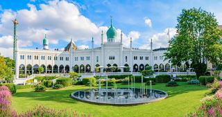 A vibrant view of Tivoli Gardens featuring lush greenery, a fountain, and charming architecture under a clear blue sky | MSC Cruises