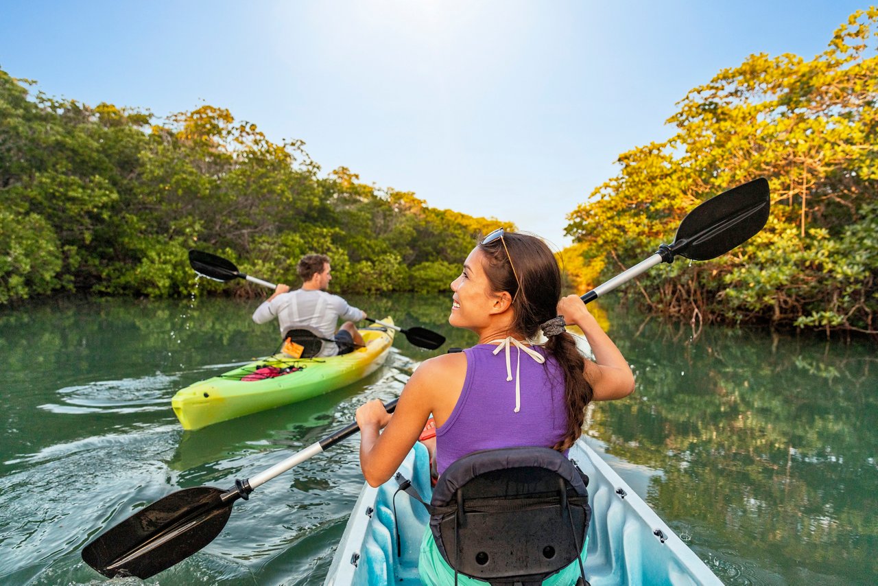A couple enjoys kayaking together on a serene river surrounded by lush vegetation and a clear blue sky | MSC Cruises