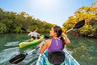 Una pareja disfruta de hacer kayak juntos en un río sereno rodeado de exuberante vegetación y un cielo azul claro | MSC Cruceros