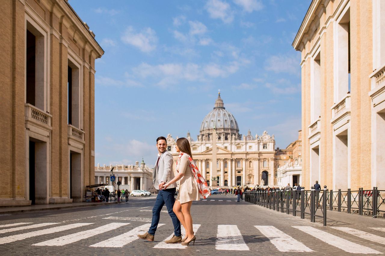 A couple walks hand in hand in a sunny street with St Peter's Basilica in the background | MSC Cruises