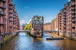 A scenic view of the canals and historic buildings in Hamburg's Speicherstadt district under a bright blue sky | MSC Cruises