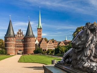 The historic Holstentor gate in Lübeck with its distinctive towers and a lion statue in the foreground | MSC Cruises