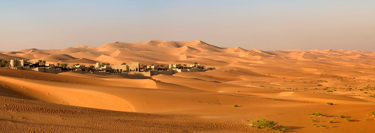 Expansive desert landscape with undulating dunes and modern architecture under a warm sky | MSC Cruises