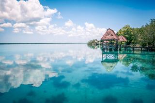 Ein ruhiger Blick auf die Bacalar-Lagune mit ruhigem Wasser, das den Himmel spiegelt, und einem charmanten Wasserbungalow | MSC Cruises