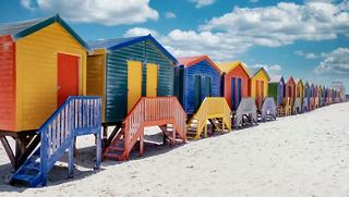 Casas de playa vibrantes bordean la playa de Muizenberg bajo un cielo brillante y una costa arenosa | MSC Cruceros