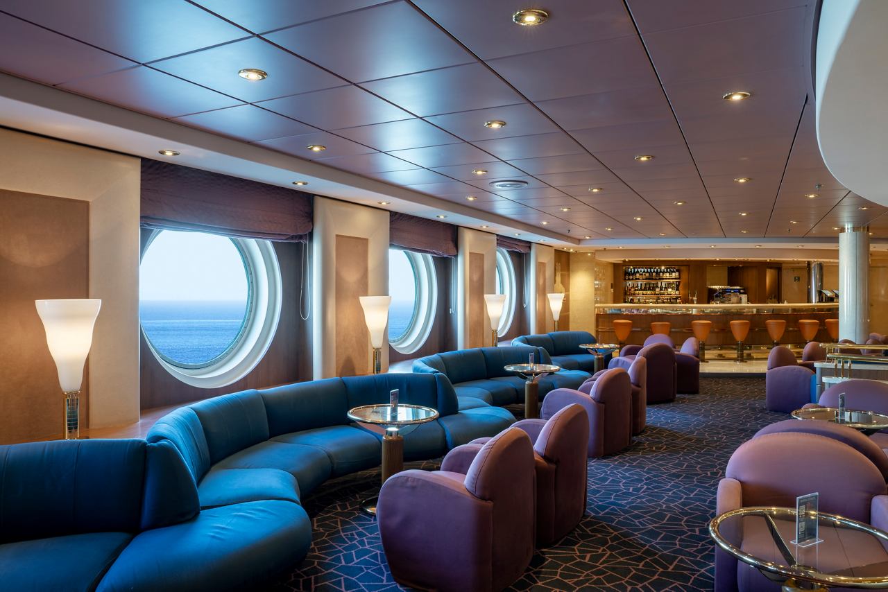 A stylish lounge area with comfortable seating and large portholes overlooking the sea | MSC Cruises
